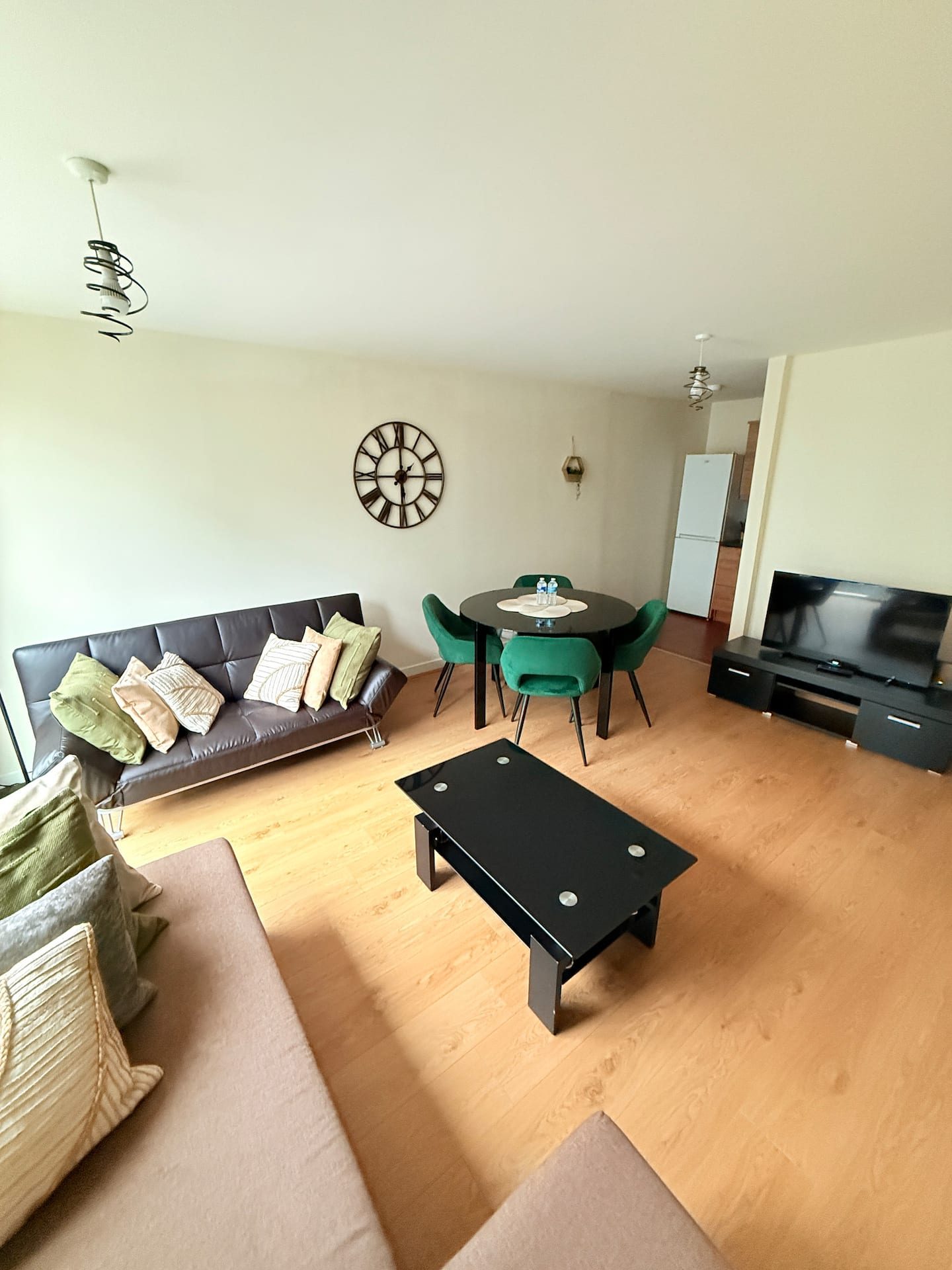 The living room at The Central Hub, with a sofa bed, a round dining table with green chairs and a television