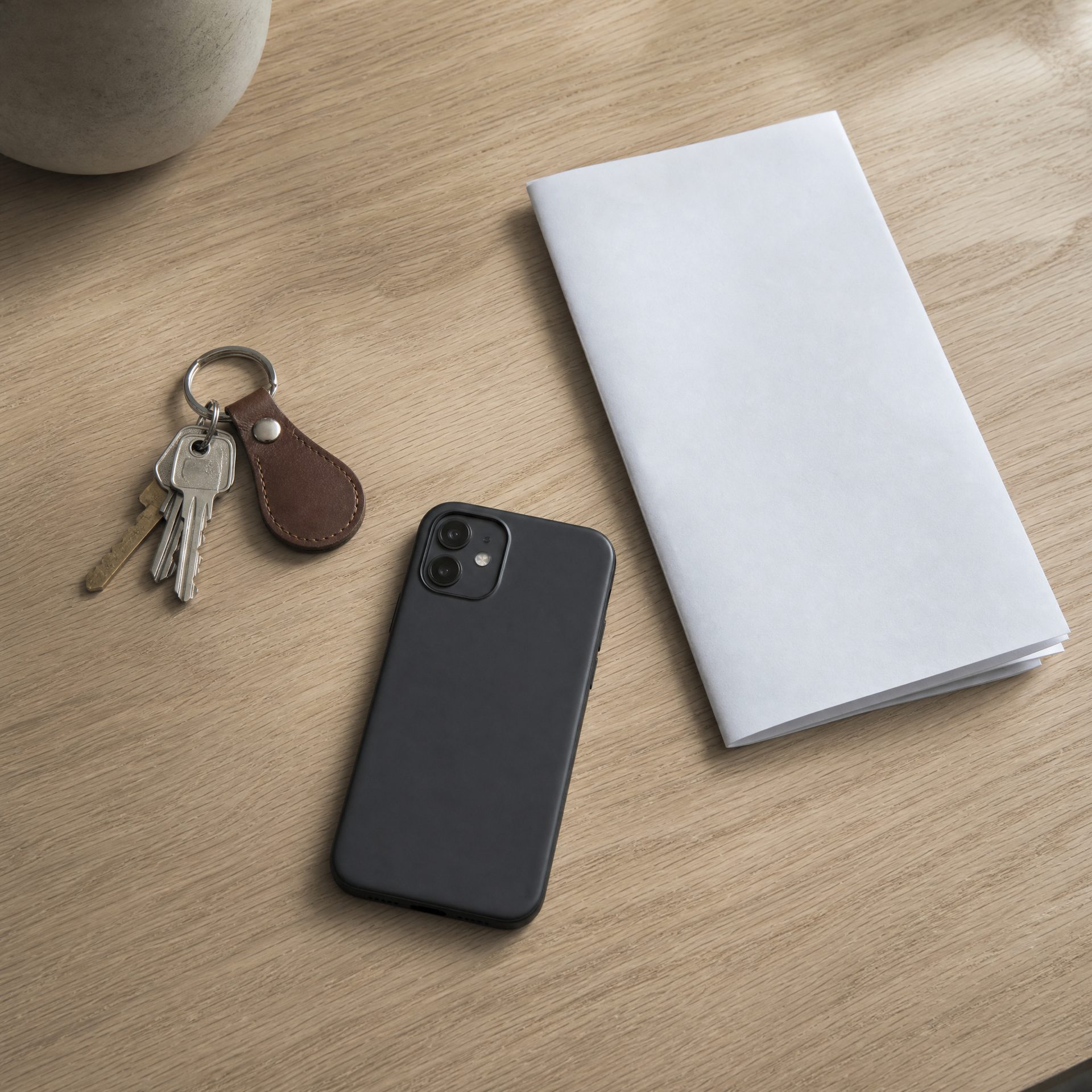 Keys on a leather fob, a phone and a folded document on an oak table